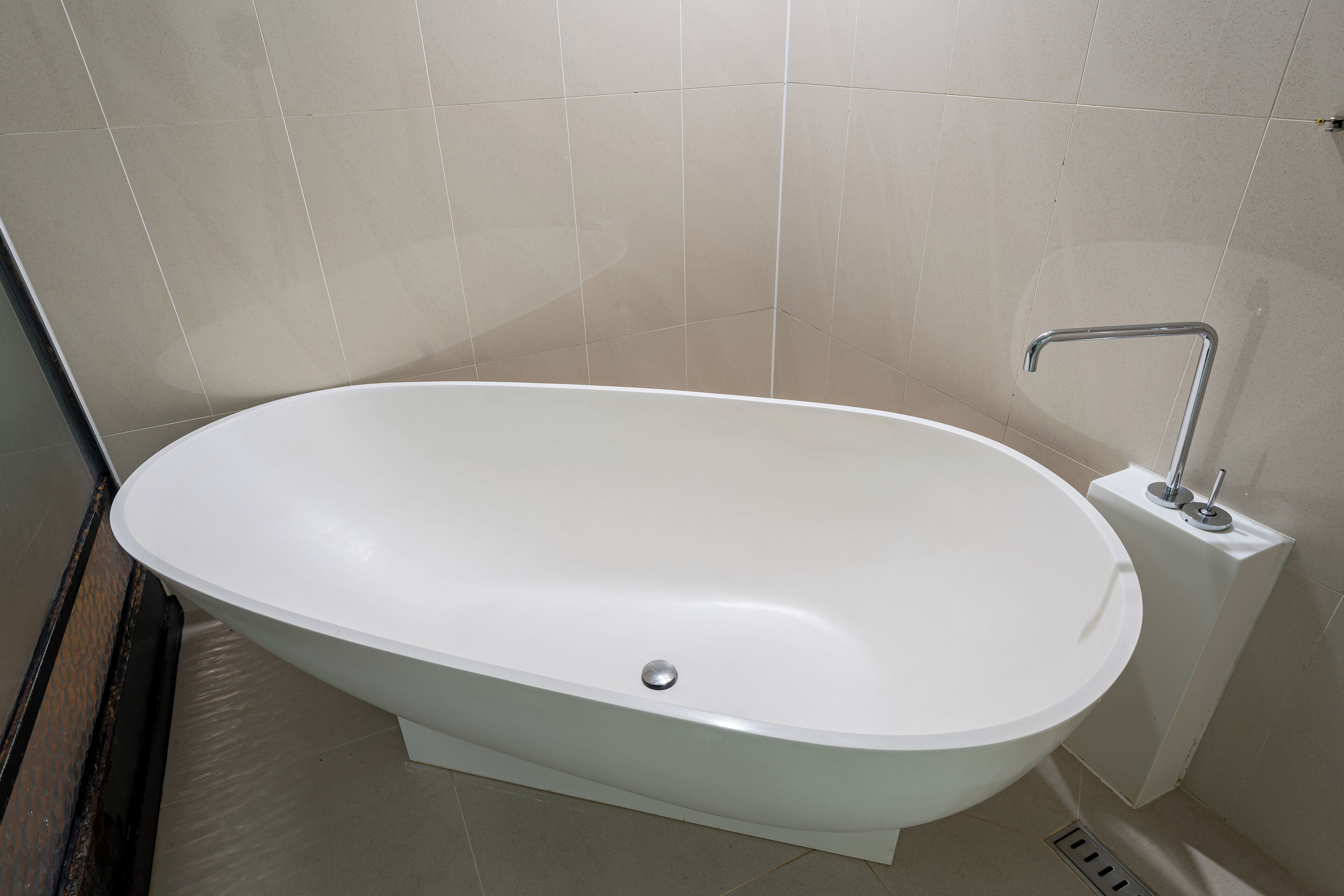 A modern bathroom with a freestanding bathtub, a wall-mounted faucet, and a tiled floor.