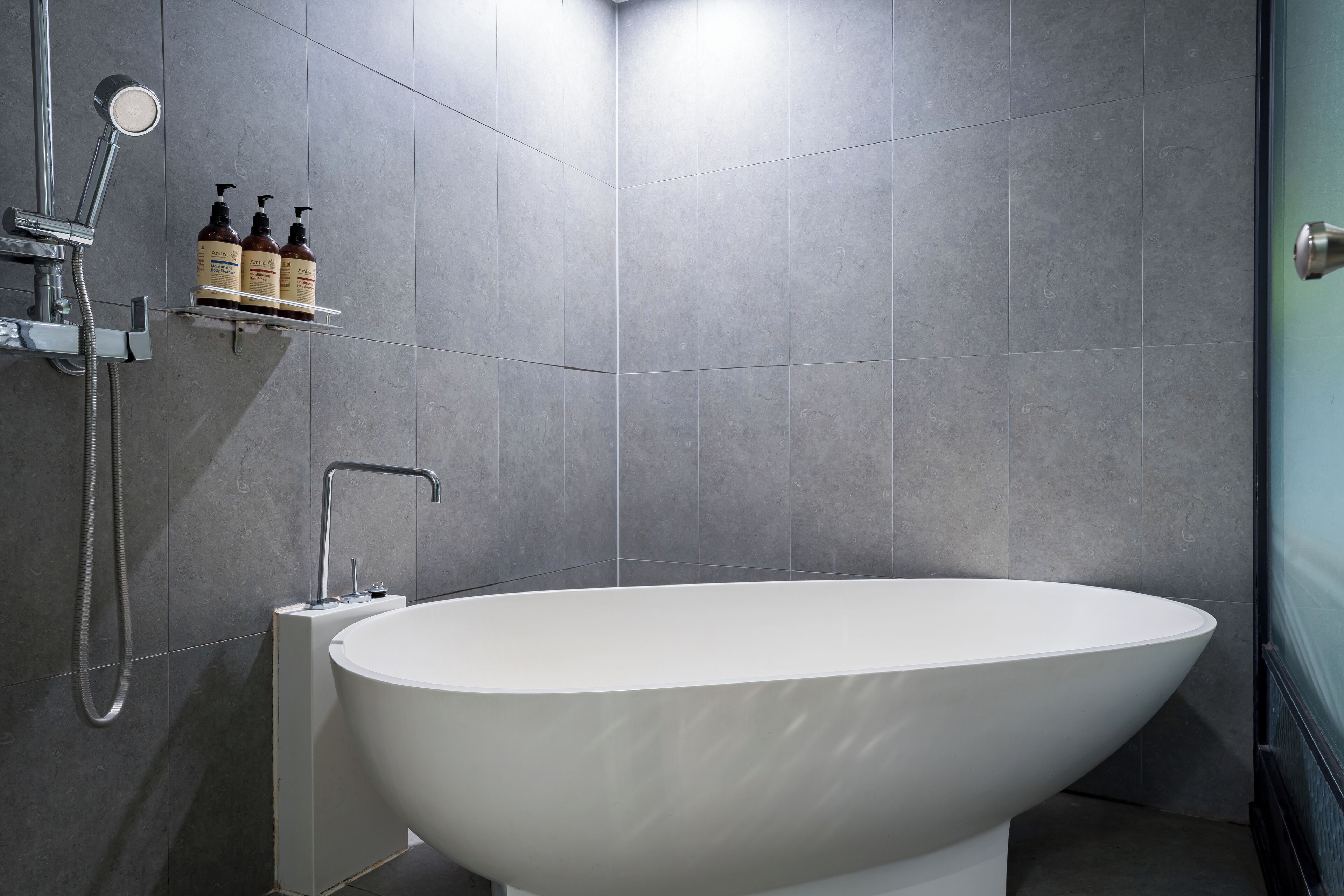 A modern bathroom with a freestanding bathtub, a showerhead, and a shelf with toiletries.