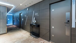 Un couloir d’hôtel moderne avec un revêtement en bois foncé, une console noire agrémentée d’un objet décoratif et une porte portant l’inscription « 5e étage, chambres 501 à 507 ».
