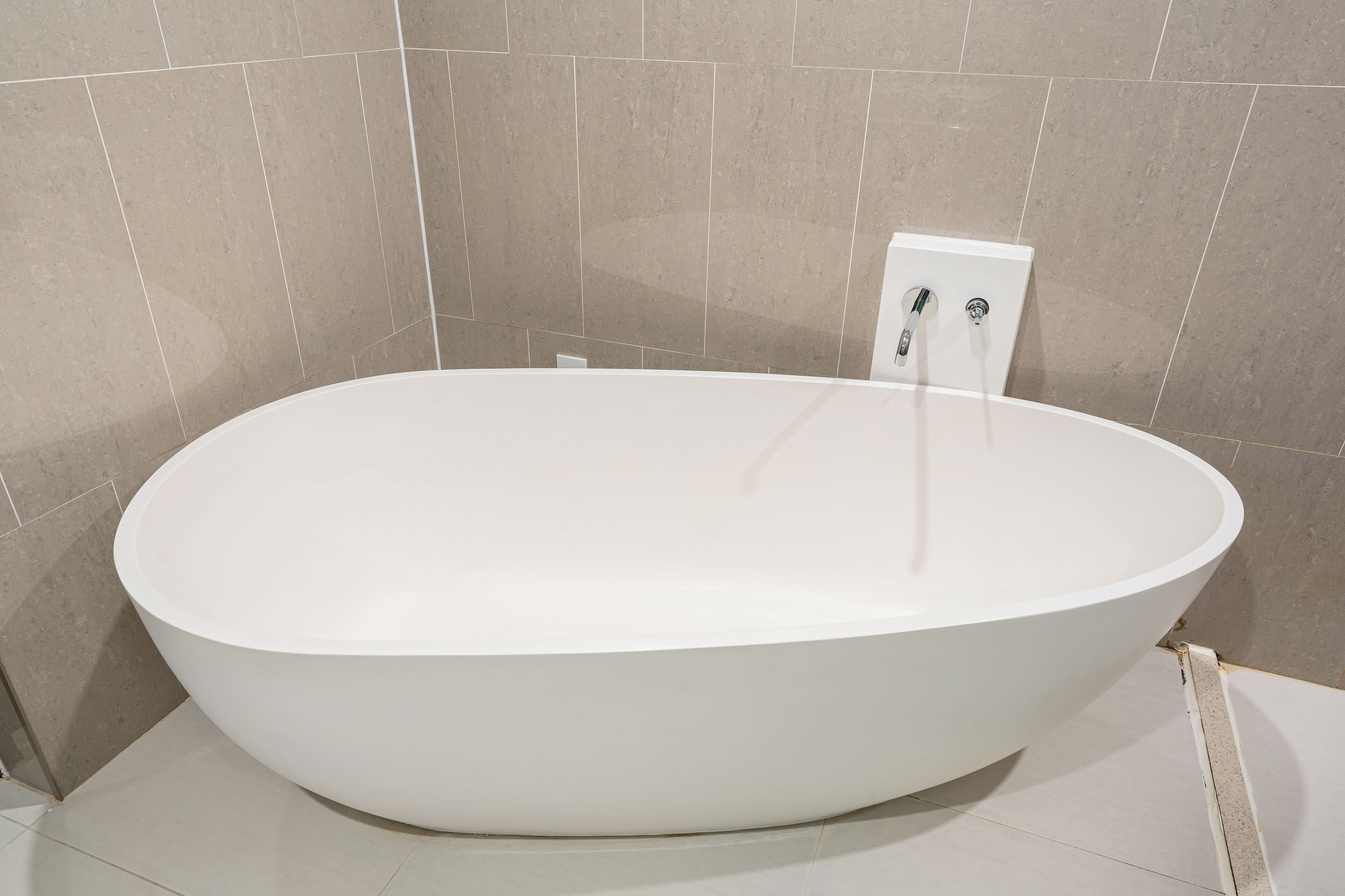Un baño moderno con una bañera independiente, paredes con azulejos y un enchufe visible.