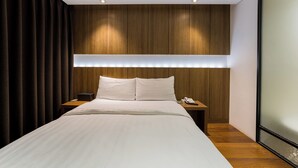 Une chambre d’hôtel moderne avec un grand lit, une tête de lit en bois, des tables de chevet et une grande fenêtre.