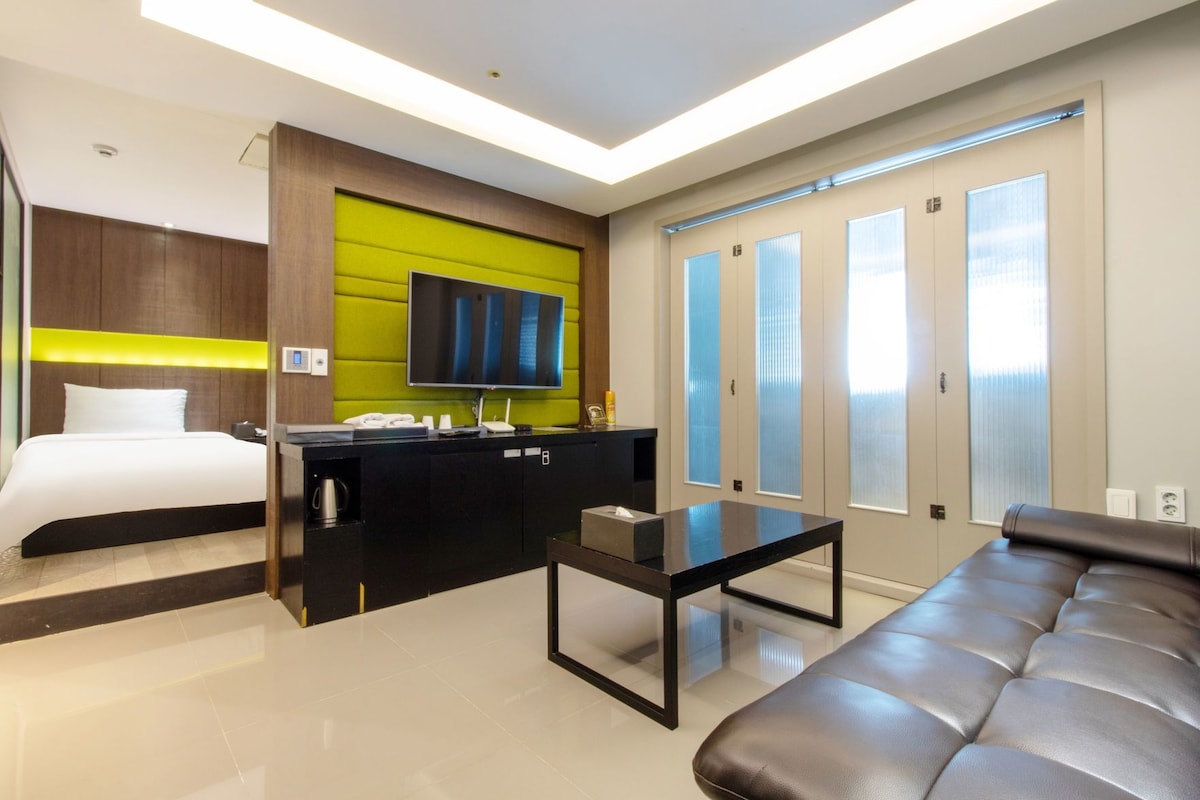 A modern hotel room with a bed, a desk, a sofa, and a TV.