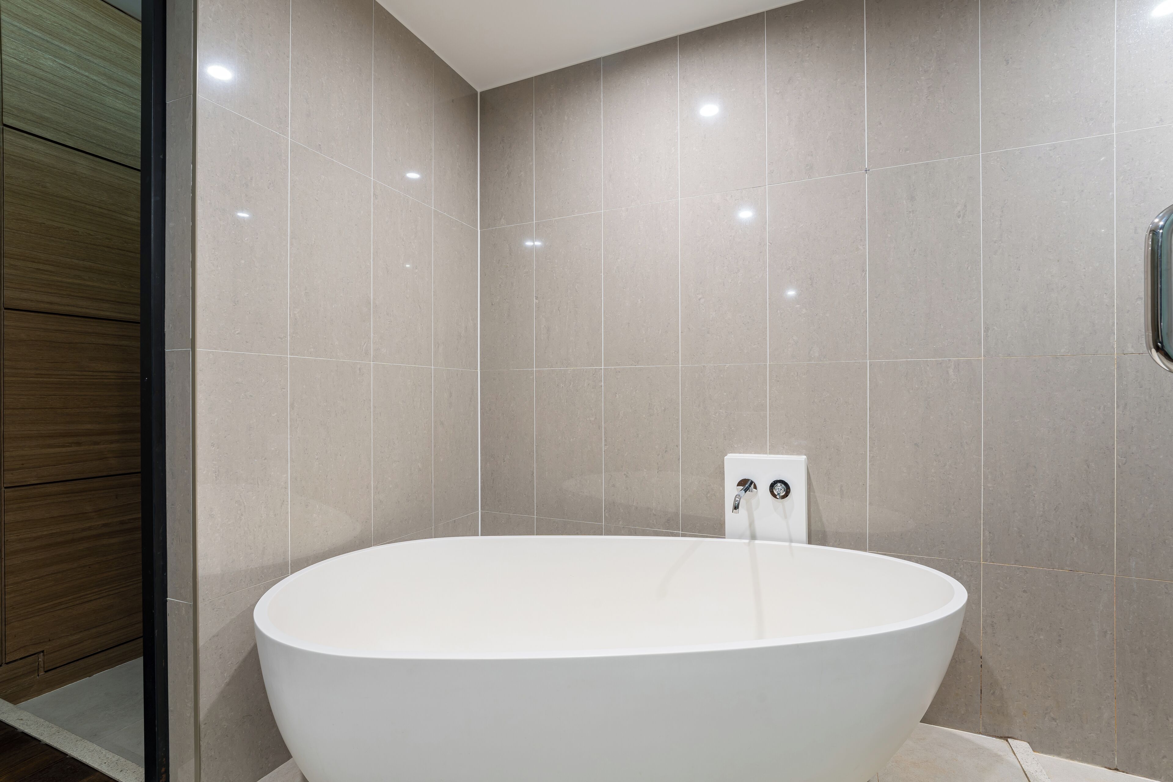 A modern bathroom with a freestanding bathtub, tiled walls, and a wooden panel on one side.