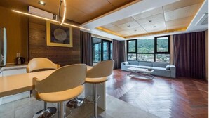 Un salon moderne avec un plancher en bois, un canapé, un coin repas comprenant une table et des chaises, et de grandes fenêtres offrant une vue dégagée.
