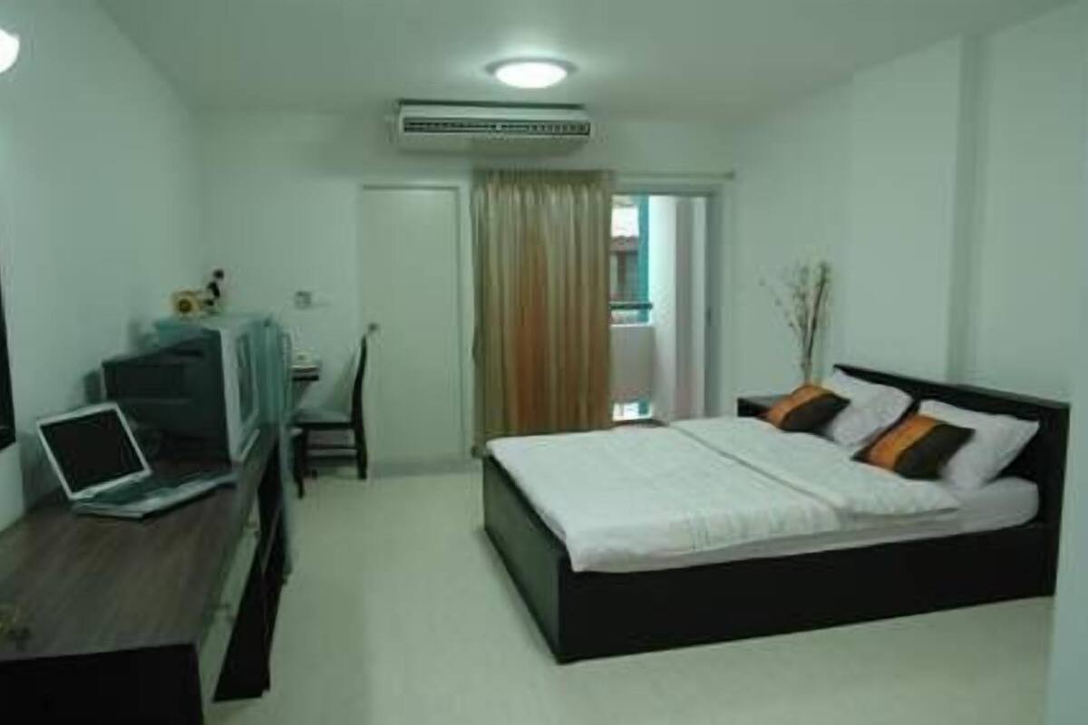 Un dormitorio con una cama, un escritorio con una computadora portátil, una silla y un ventanal con cortinas.