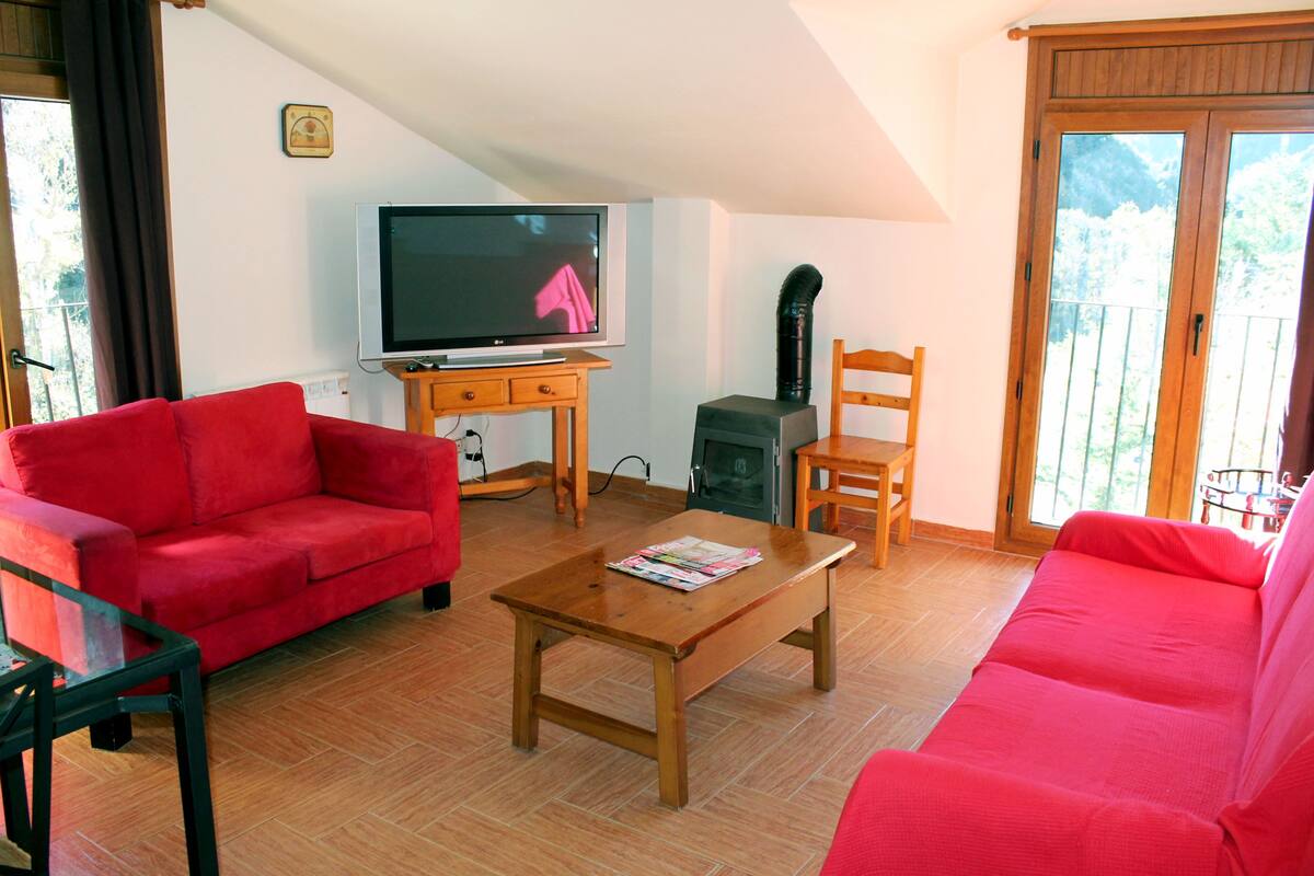 A living room with a red sofa, a wooden coffee table, a television, and a fireplace.