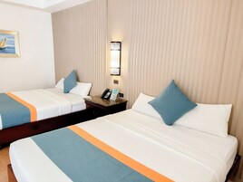 Habitación de hotel con dos camas, cada una con colcha azul y naranja, una mesita de noche con teléfono y lámpara, y una lámpara de pared.
