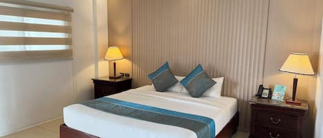 Een hotelkamer met een bed, twee nachtkastjes met lampen, een telefoon en een bedieningspaneel aan de muur.