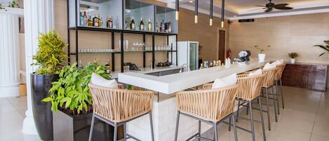 A bar area with a long counter, wicker chairs, a large potted plant, and a glass display case with bottles.