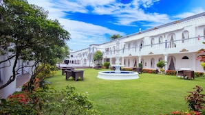 A courtyard with a fountain, outdoor seating, and a white building with arches.