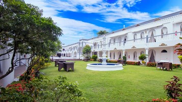 Un patio con una fuente, mobiliario exterior y un edificio blanco con arcos.