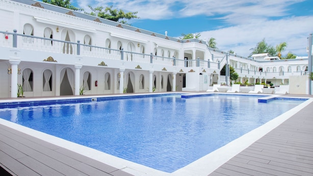 A large rectangular swimming pool with a tiled edge, surrounded by a white building with arched windows and balconies.