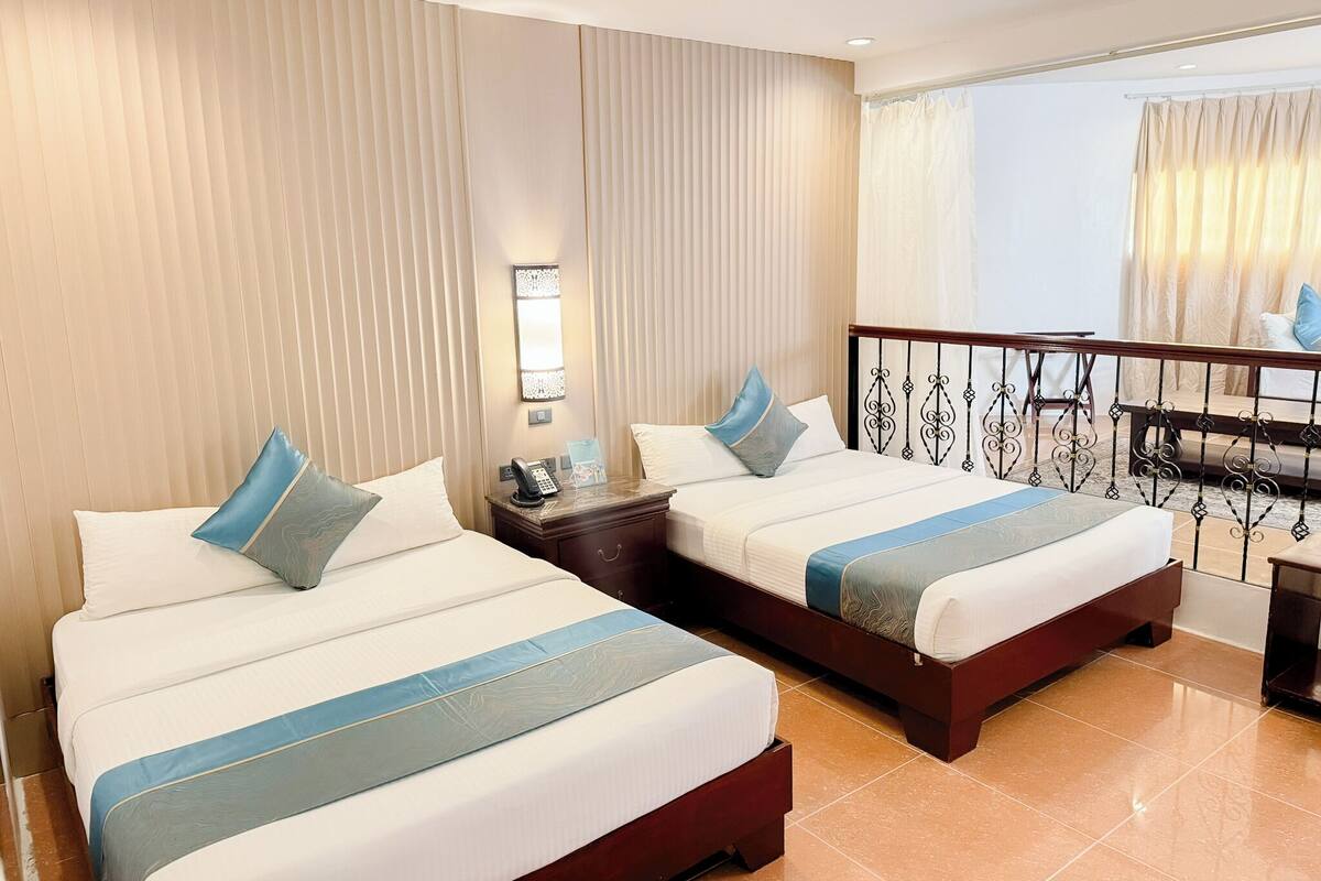 A hotel room with two beds, a nightstand, a phone, a lamp, and a view of the outside.