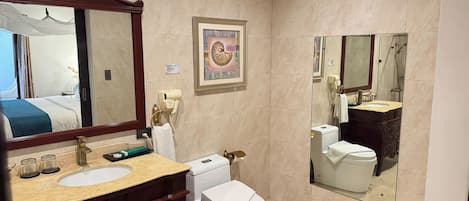 A hotel bathroom with a large mirror, a sink, a toilet, a hairdryer, and a framed picture on the wall.