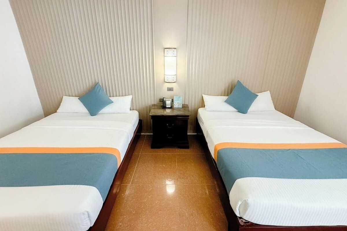 Een hotelkamer met twee bedden, een nachtkastje, een wandlamp en een betegelde vloer.
