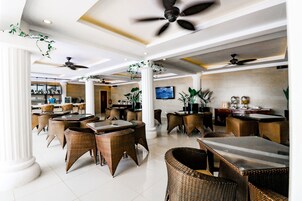 Un espacio interior amplio con varias mesas y sillas, ventiladores de techo y plantas en macetas.