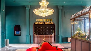Un hall con un sillón rojo, una araña y un mostrador de recepción.