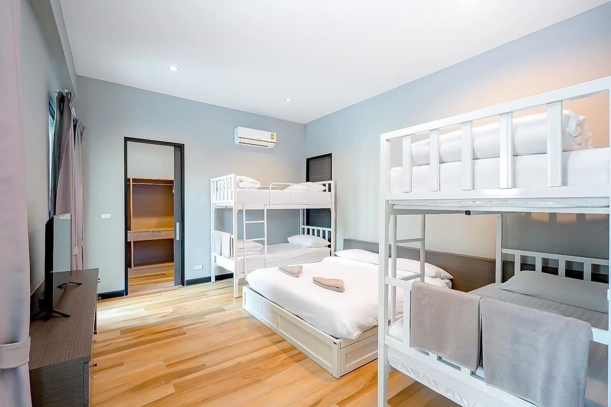 A room with bunk beds, a wooden floor, a wardrobe, and an air conditioning unit.