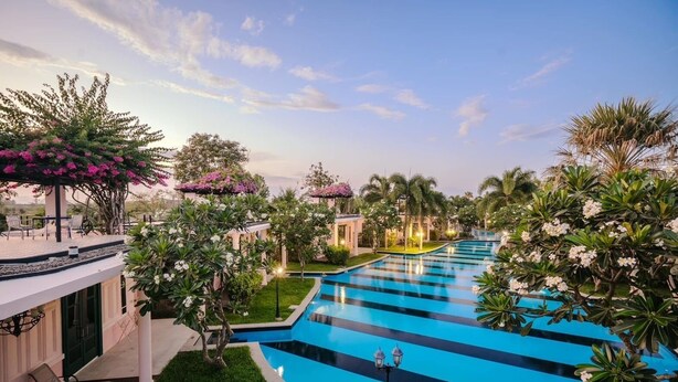 Una piscina con diseño azul y blanco a rayas, rodeada de abundante follaje y palmeras.