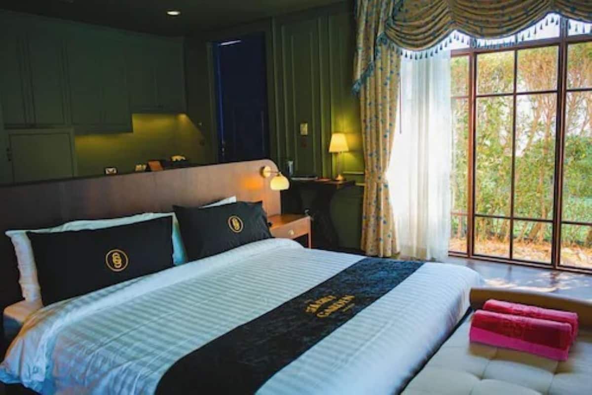 A hotel room with a large bed, a nightstand, a lamp, and a window with a view of trees.