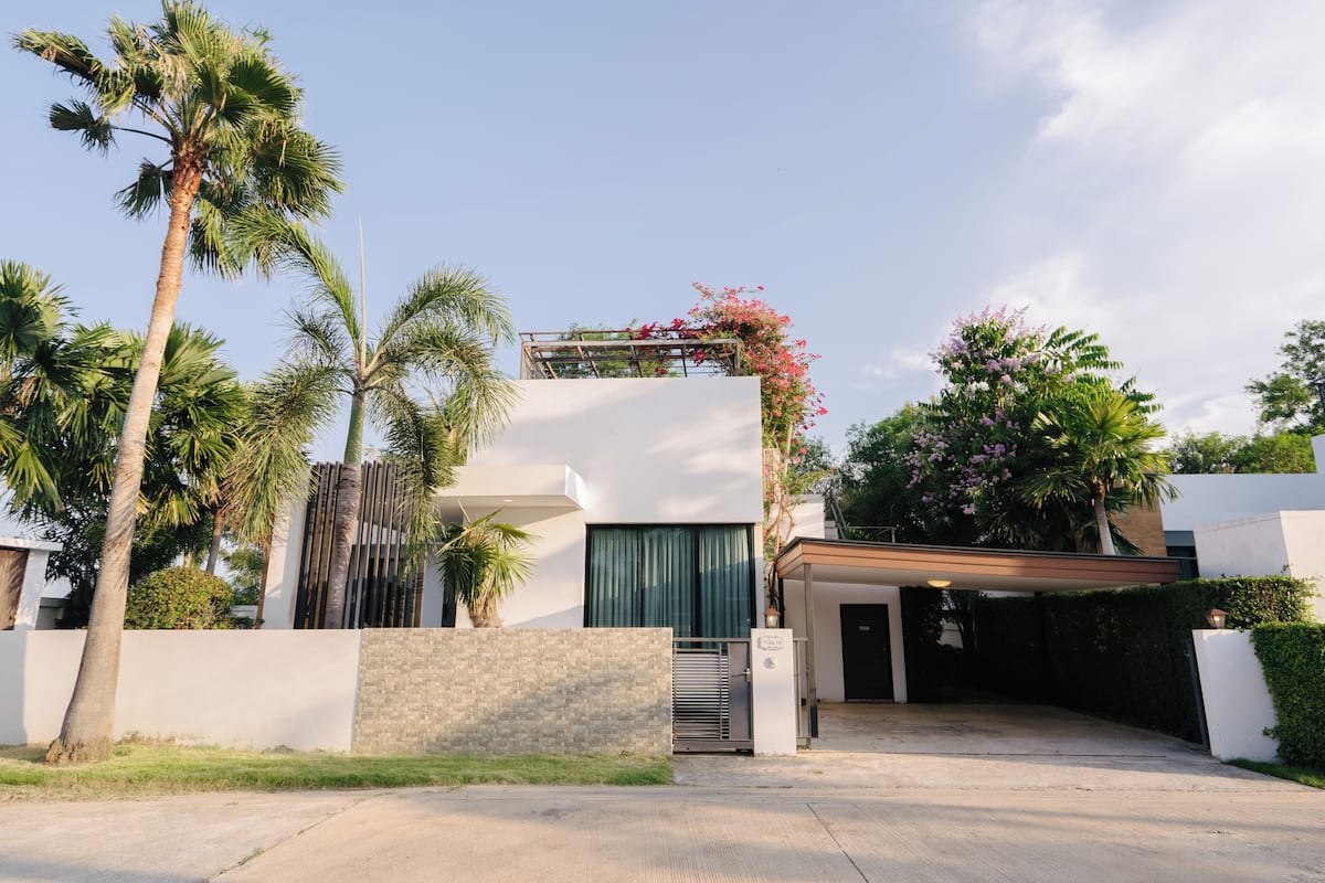 A modern house with a covered driveway, palm trees, and a white wall.