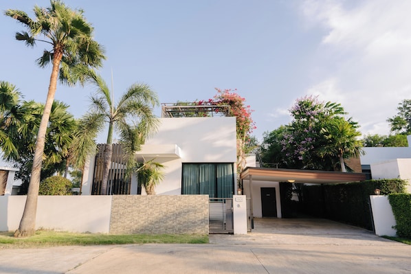 A modern house with a covered driveway, palm trees, and a white wall.