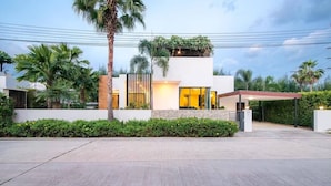 Un edificio moderno con un área exterior cubierta, rodeado de follaje y palmeras.