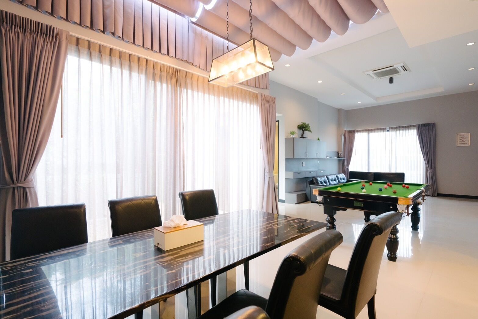 A modern room with a pool table, a dining table with chairs, and a sofa.