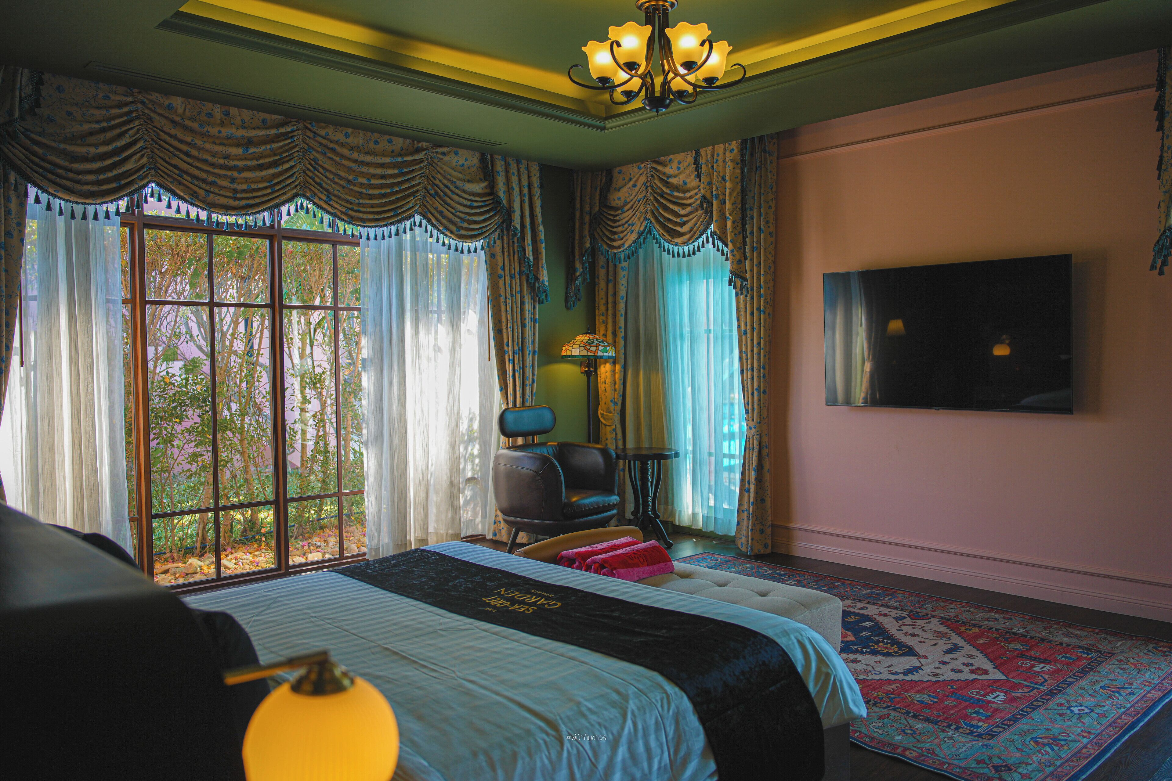 A bedroom with a large bed, a television on the wall, a chair, and a window with curtains.