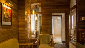 A cozy room with wooden walls and ceiling, a wooden table, a sofa, and a fireplace. - Central Heritage Resort & Spa, Darjeeling (Darjeeling)