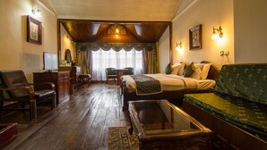 A hotel room with a wooden floor, a bed with a green upholstered headboard, a sofa, a desk with a computer, and a chair. - Central Heritage Resort & Spa, Darjeeling (Darjeeling)