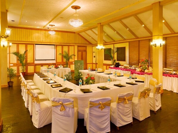 Une salle de banquet avec des tables rondes, des nappes blanches et des rubans dorés sur les chaises.