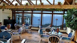 A spacious indoor area with wicker furniture and large windows offering mountain views. - Central Heritage Resort & Spa, Darjeeling (Darjeeling)