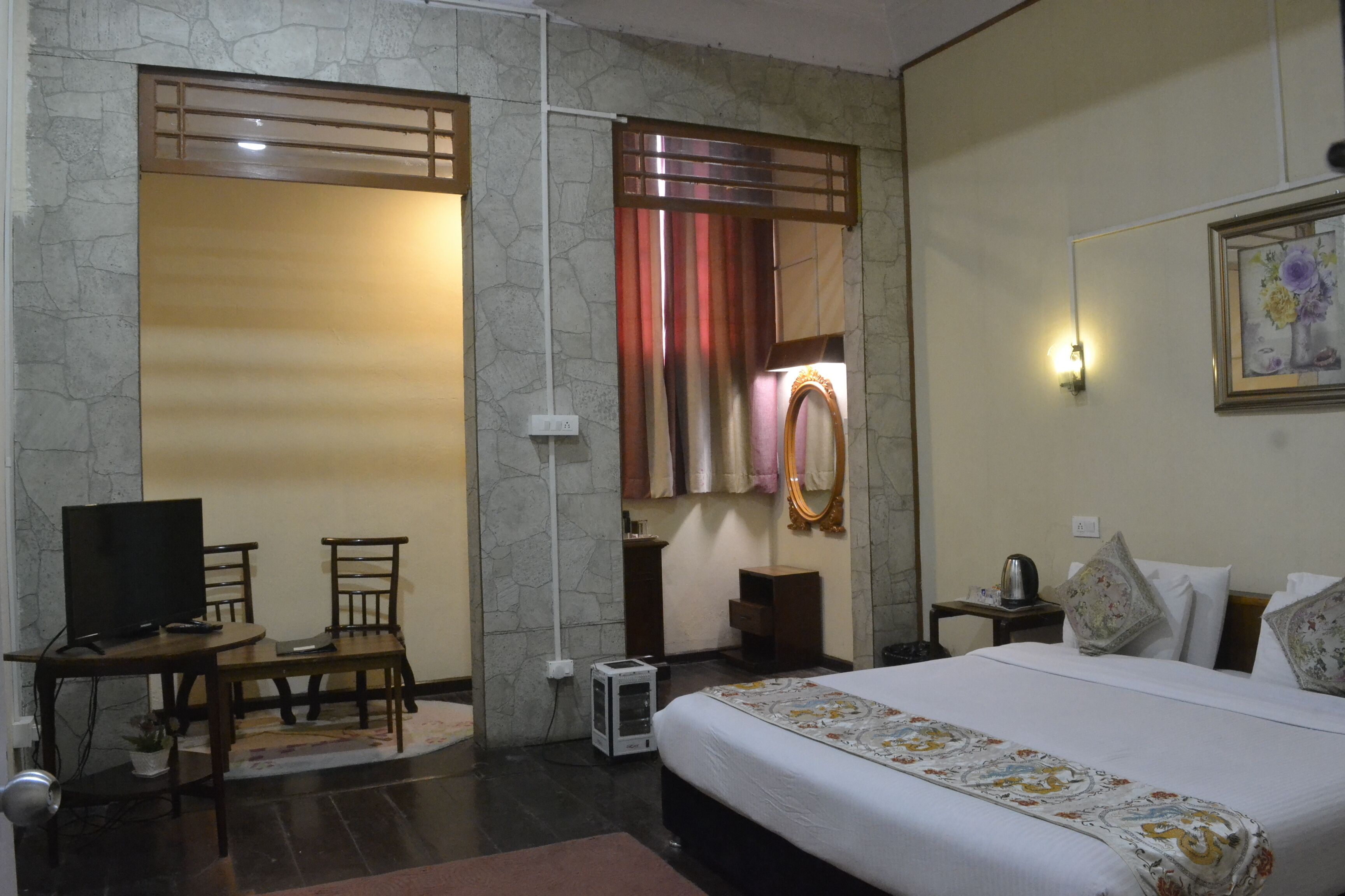 A hotel room with a bed, a desk with a chair, a television, and a mirror.