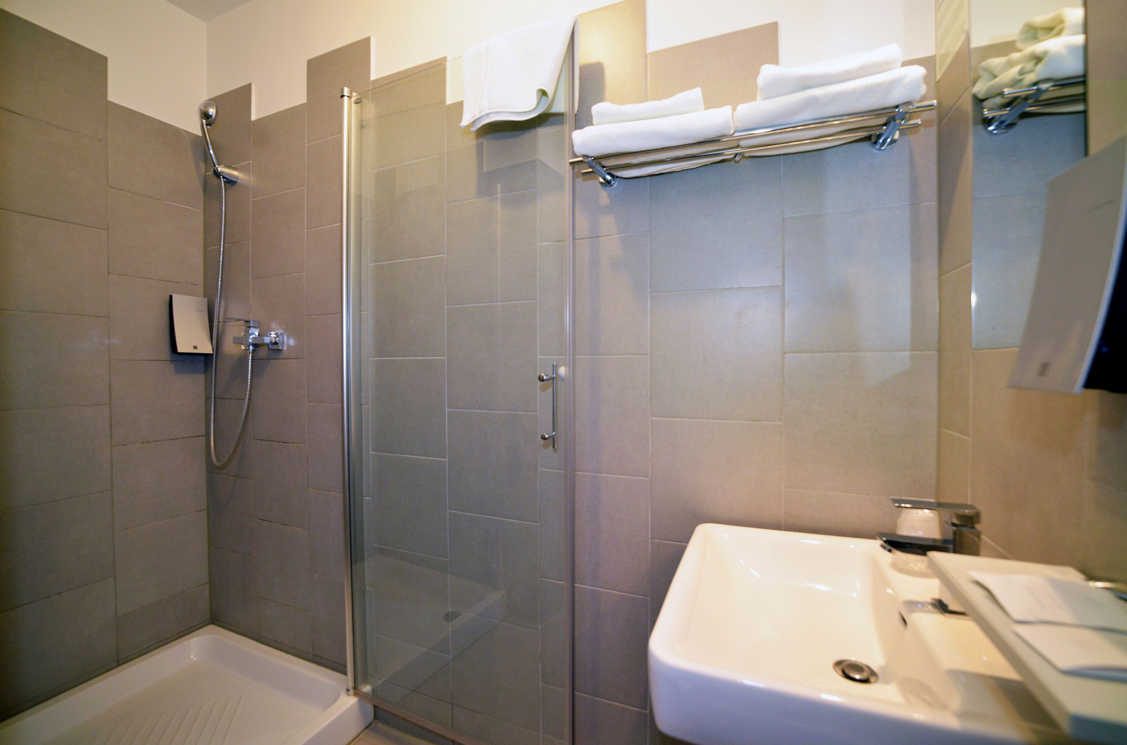 Een moderne badkamer met een douchecabine van glas, een witte wastafel en keurig opgevouwen handdoeken.