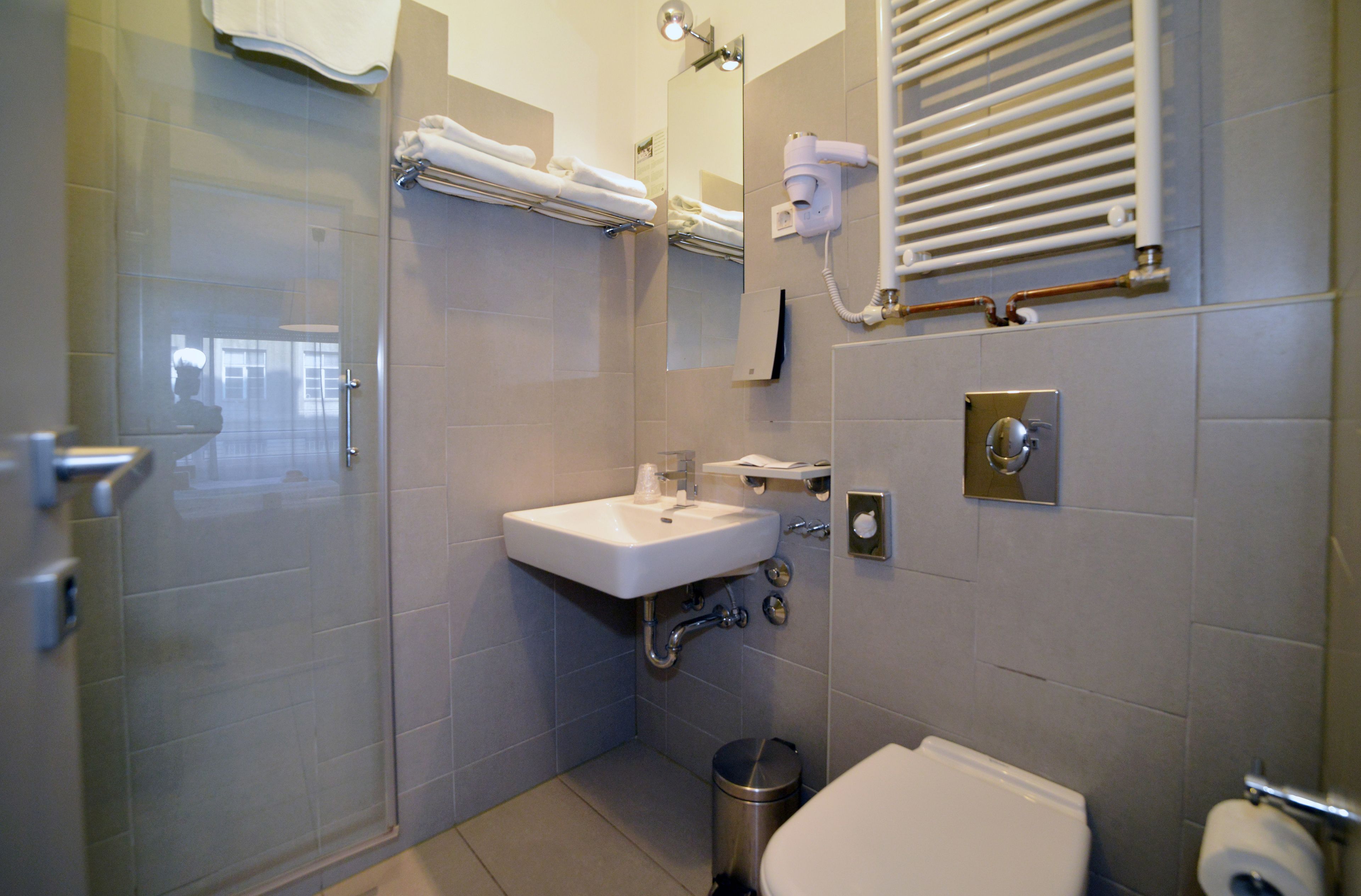 A bathroom with a glass shower enclosure, a sink, a toilet, a trash can, and a towel rack with towels.
