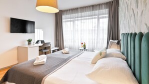 Una habitación de hotel con cama, escritorio, silla, televisor y ventana con cortinas.