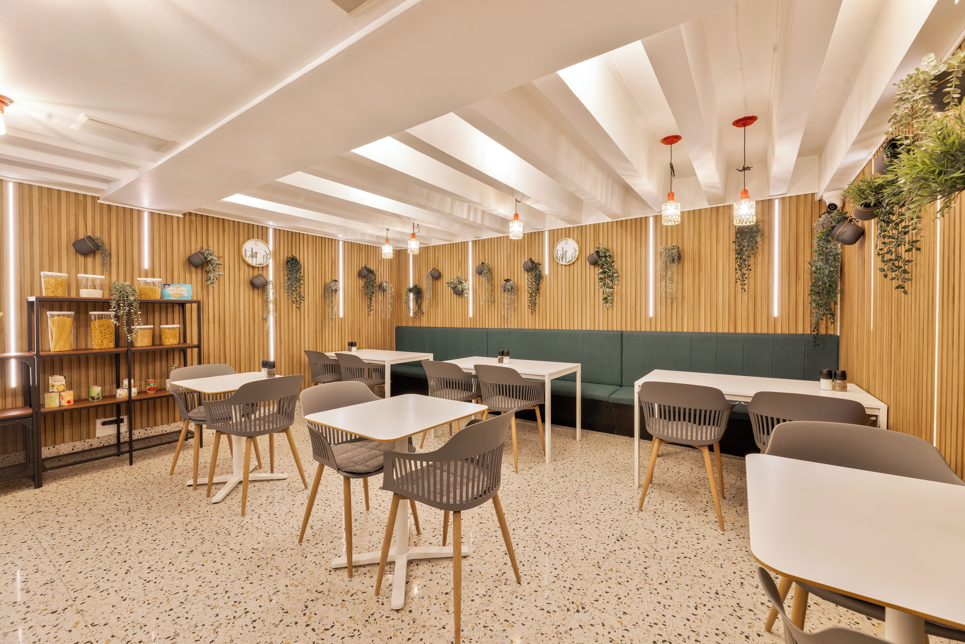 Interior modern d'un restaurant amb parets revestides de fusta, diverses taules i cadires, plantes penjants i lluminàries pendents.