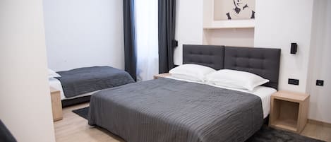 A modern hotel room with a large bed, a smaller bed, a bedside table, a nightstand, a black rug, and a wall-mounted air conditioning unit.