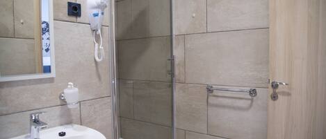 Une salle de bain équipée d’un lavabo, d’un miroir, d’un sèche-cheveux et d’une douche.