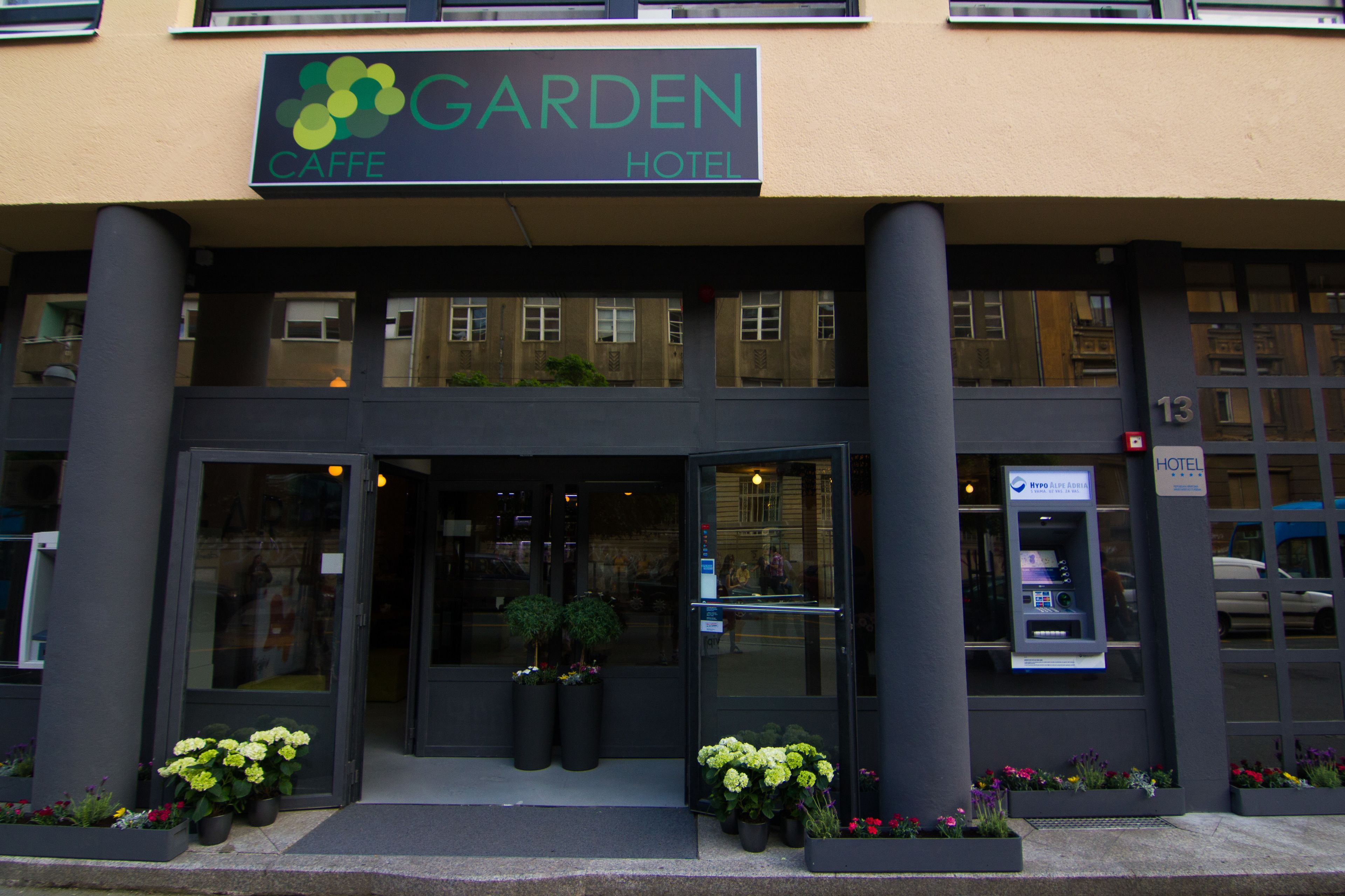 Entrada de un hotel con un cartel que dice "Garden Hotel" y un cajero automático visible.