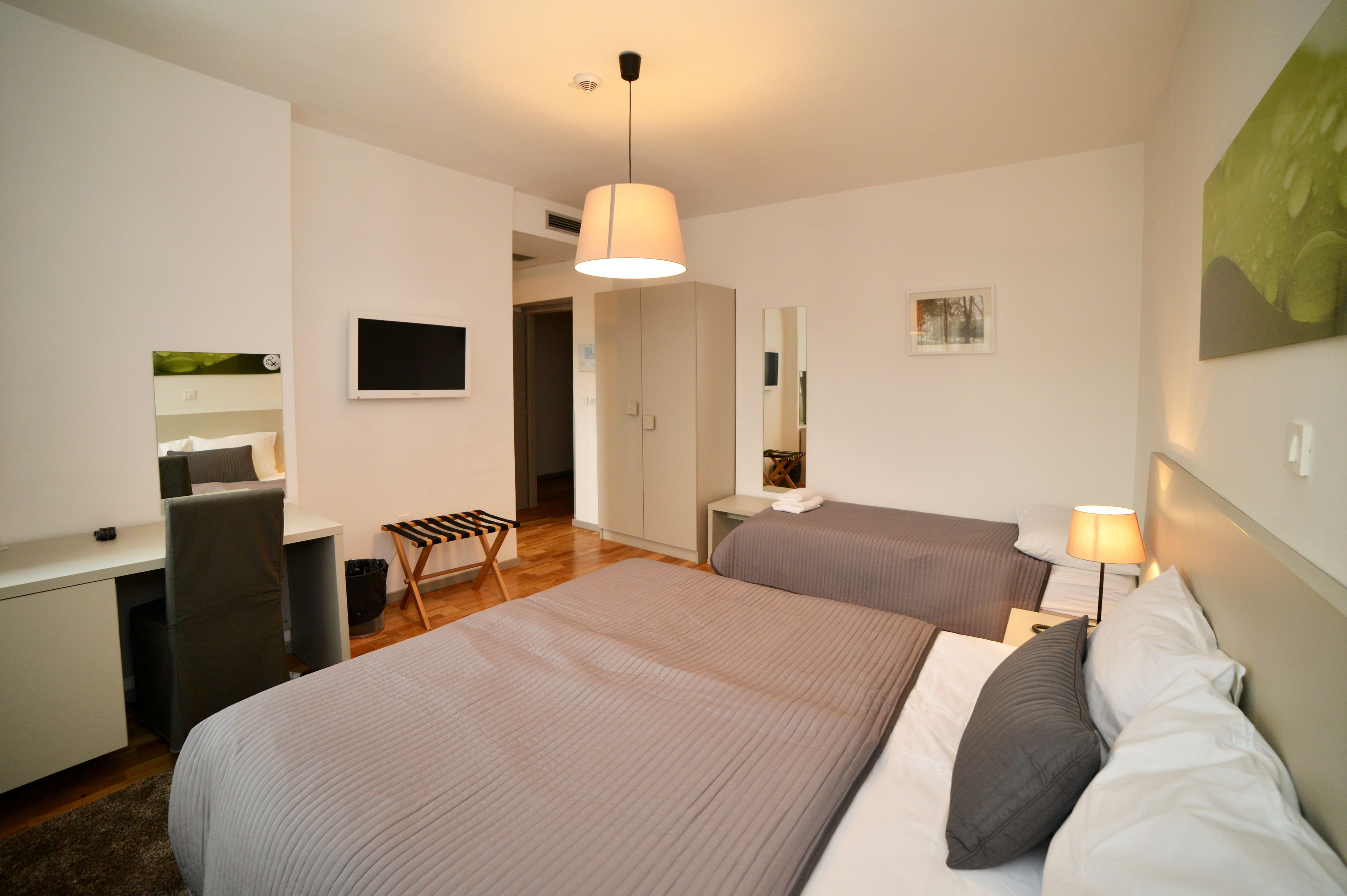 Una habitación de hotel moderna con dos camas, un escritorio, una silla, un televisor y un espejo.