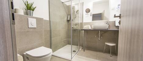 A modern bathroom with a glass-enclosed shower, a toilet, a sink, and a small stool.