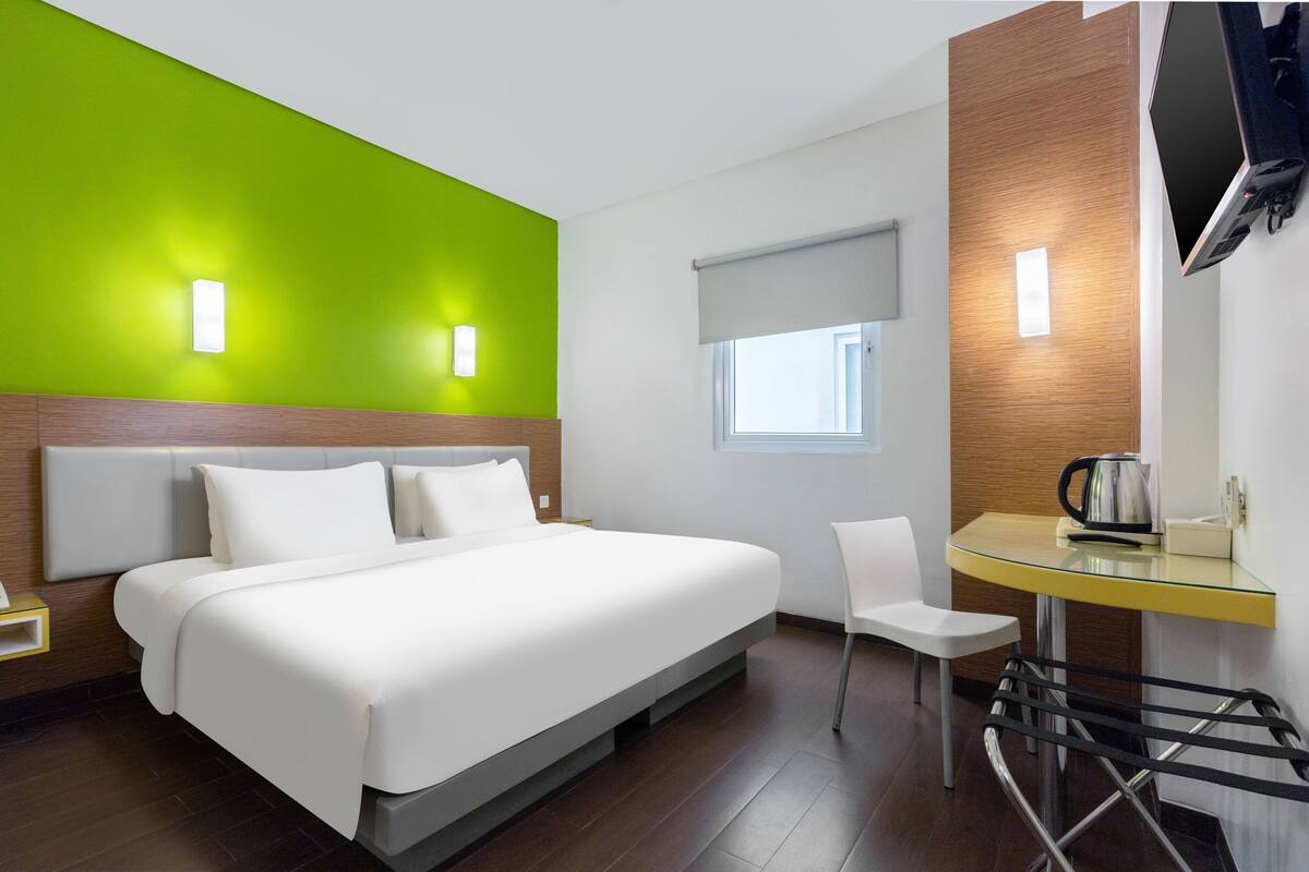 A modern hotel room with a large bed, a small desk, a chair, and a television mounted on the wall.