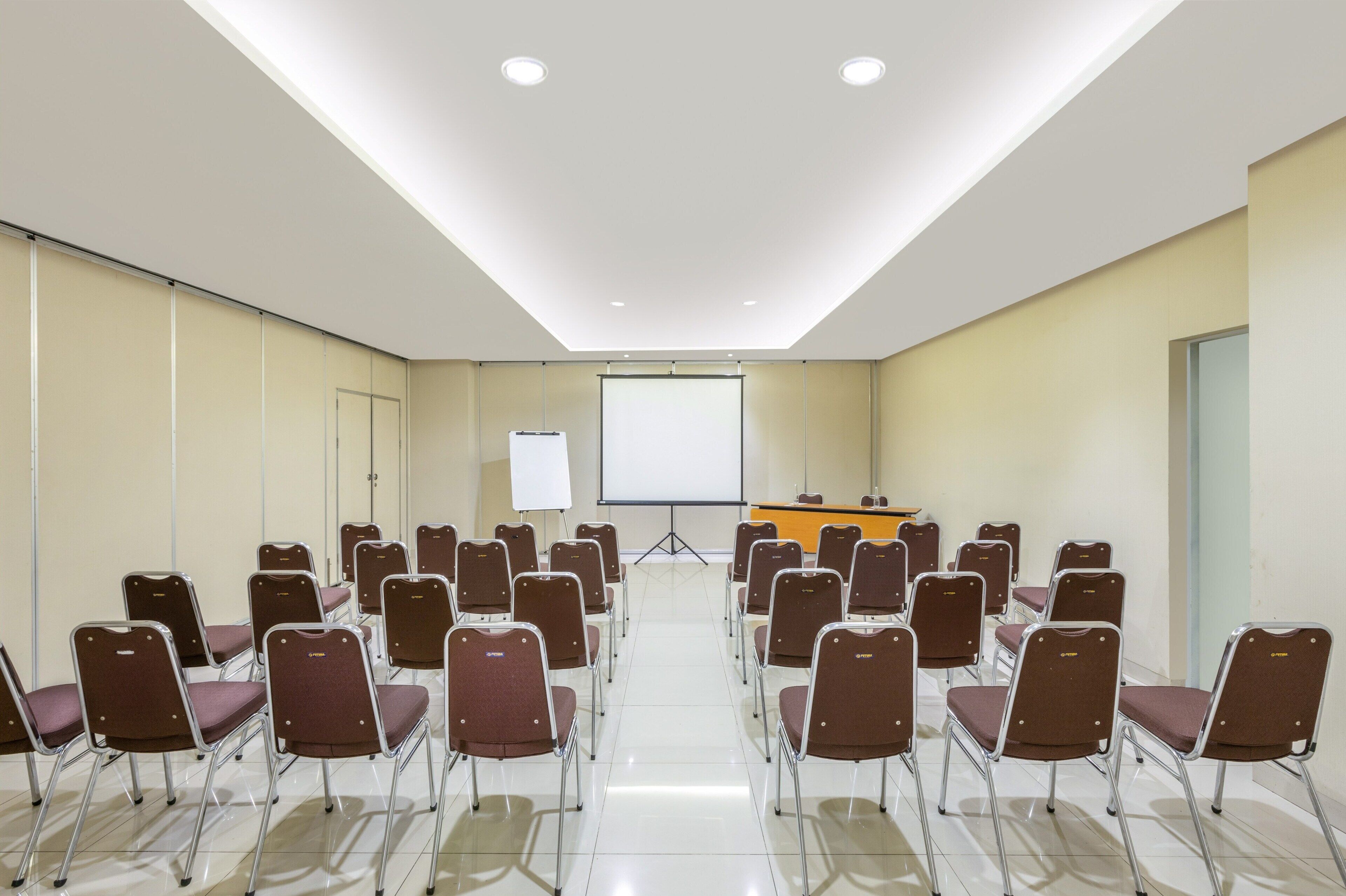 A conference room with rows of brown chairs, a whiteboard, and a presentation screen.