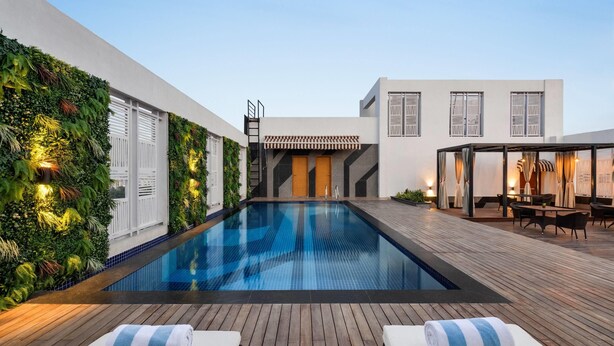 Piscina com espreguiçadeiras de madeira, um edifício branco com persianas e uma parede de jardim vertical.