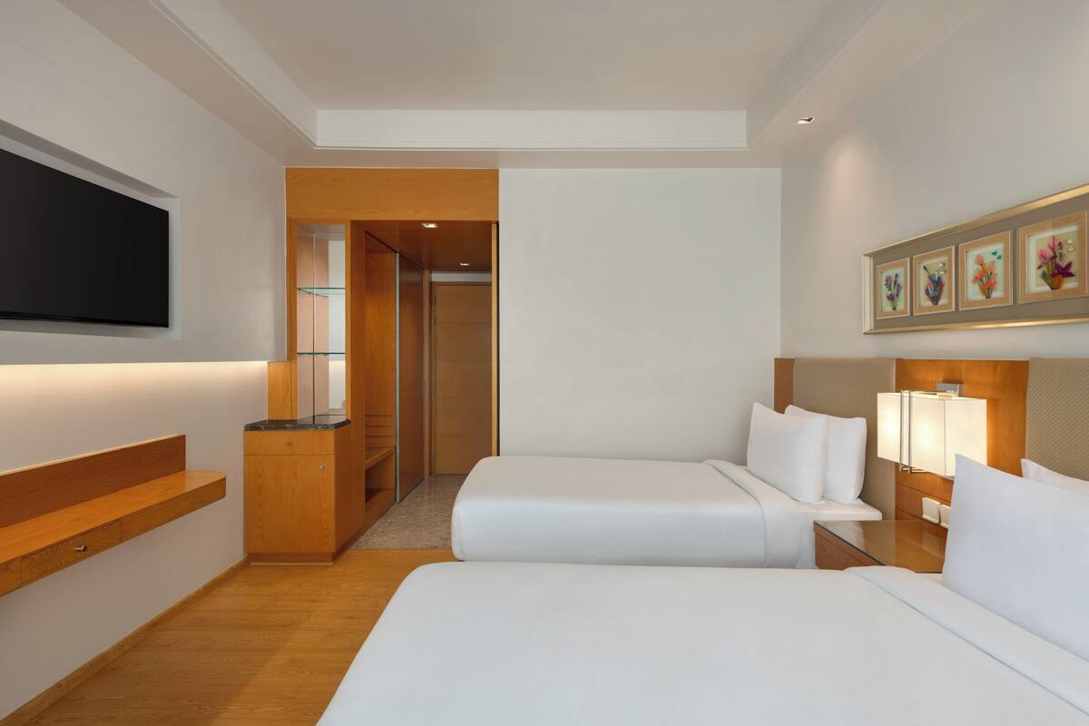 A hotel room with two beds, a TV, a wooden cabinet, a desk, and a framed picture on the wall.