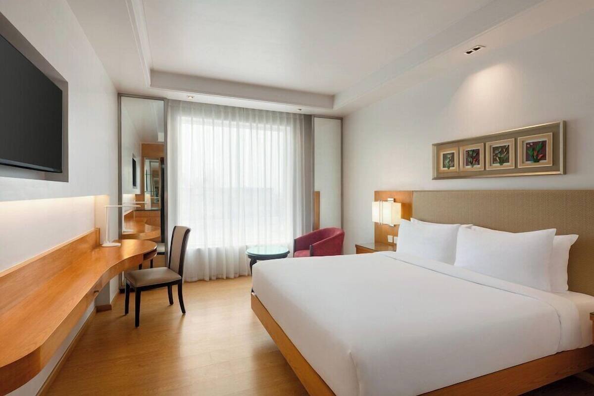 A hotel room with a bed, a desk, a chair, a TV, and a window with curtains.
