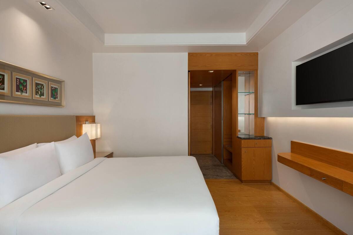 A hotel room with a large bed, a TV mounted on the wall, and a wooden desk.