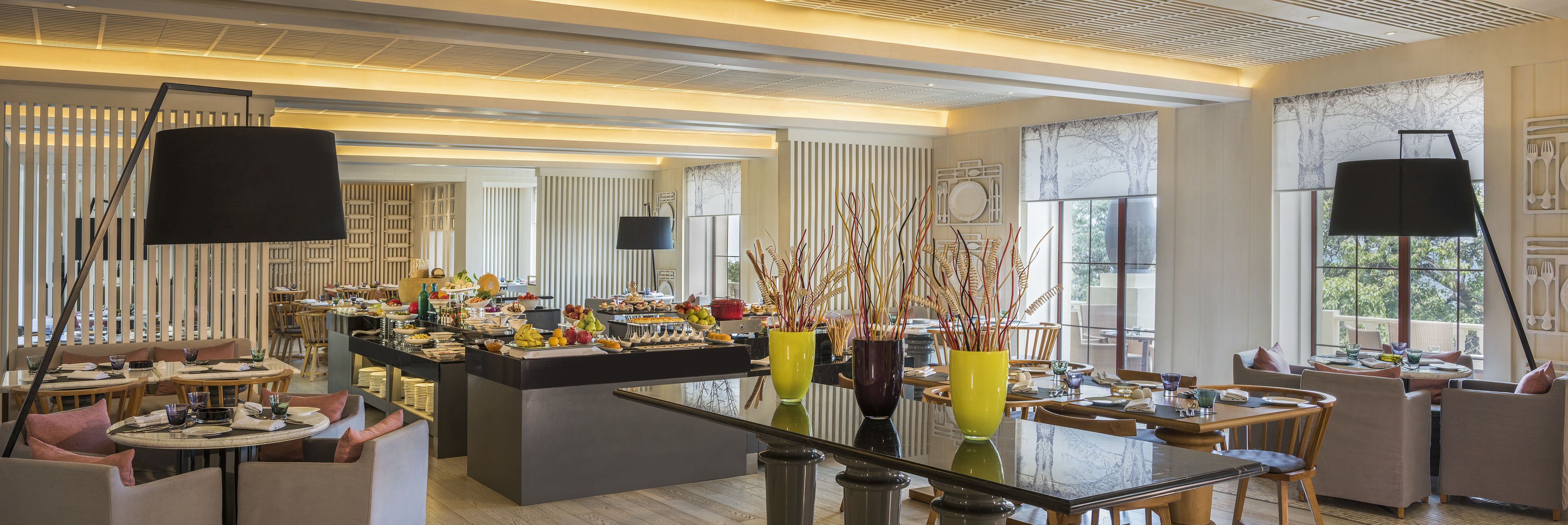 A modern dining area with a central buffet, seating arrangements, and large windows providing natural light.